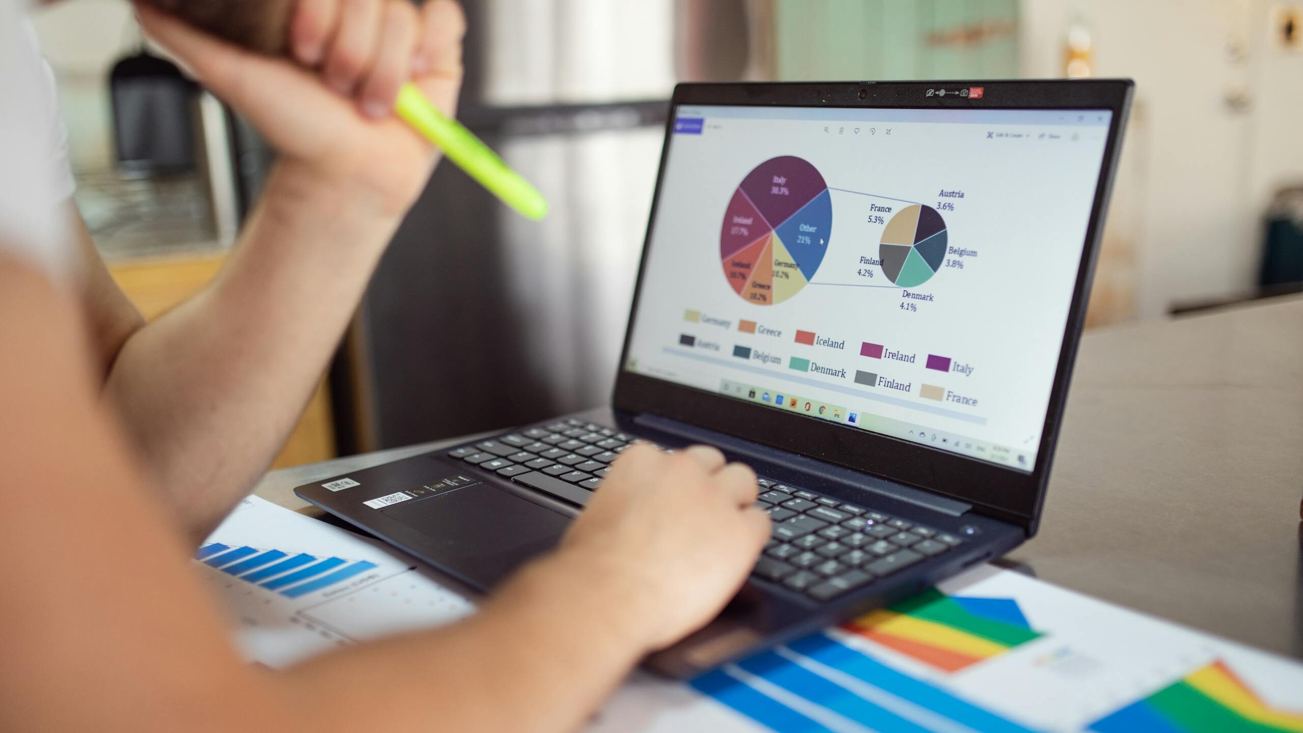 Person analyzing financial charts and graphs on a laptop with colorful documents, showcasing market analysis.